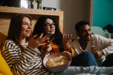 Téléchargez les photos : Un groupe d'amis regarde un film comique assis sur des sacs de haricots mous avec des boissons et des collations. - en image libre de droit