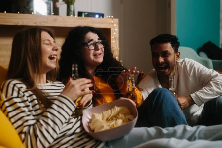 Téléchargez les photos : Un groupe d'amis regarde un film comique assis sur des sacs de haricots mous avec des boissons et des collations. - en image libre de droit