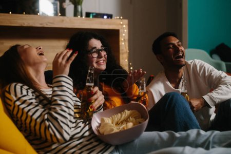 Foto de Un grupo de amigos ve una película de comedia sentados en bolsas de frijoles blandos con bebidas y aperitivos. - Imagen libre de derechos