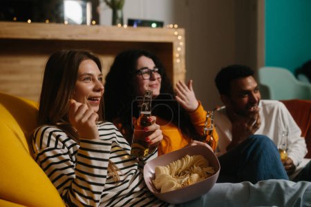 Foto de Un grupo de amigos ve una película de comedia sentados en bolsas de frijoles blandos con bebidas y aperitivos. - Imagen libre de derechos