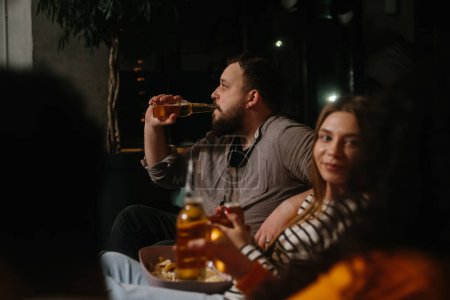 Téléchargez les photos : Un groupe d'amis s'amusent ensemble dans un café le soir, boivent de la bière et discutent. - en image libre de droit