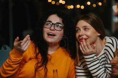 Foto de Dos amigas están viendo emocionalmente una película y comiendo papas fritas mientras están sentadas en bolsas de frijoles. - Imagen libre de derechos