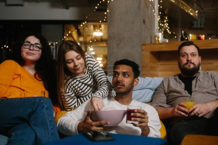 Foto de Un grupo de amigos come bocadillos y bebe cerveza mientras ven la televisión. - Imagen libre de derechos