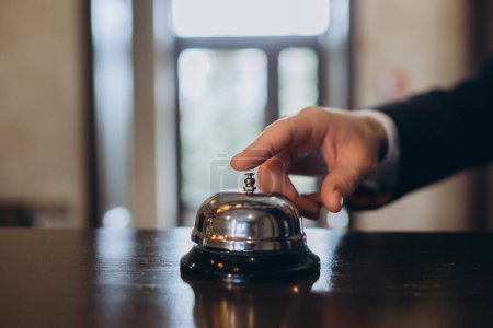 Photo for Arrival at the hotel. A man ringing a hotel reception service bell to attract attention. - Royalty Free Image