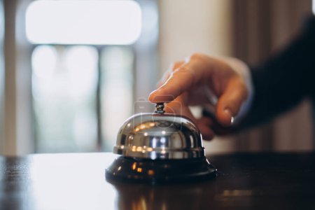 Foto de Llegada al hotel. Un hombre tocando una campana de recepción del hotel para llamar la atención. - Imagen libre de derechos
