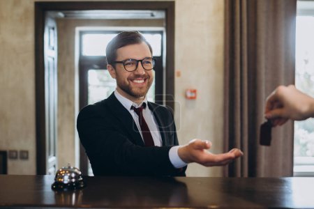 Photo for Smiling businessman takes door key after checking in hotel, selective focus. - Royalty Free Image