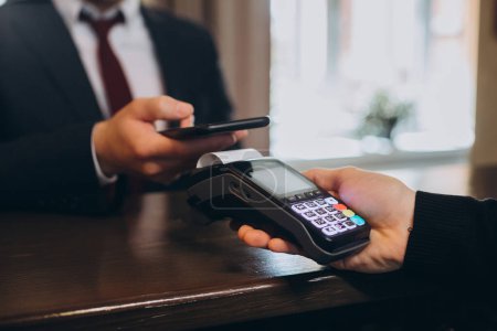 Foto de Un hombre de negocios paga una factura por una habitación de hotel a través de un teléfono inteligente con tecnología NFC. - Imagen libre de derechos