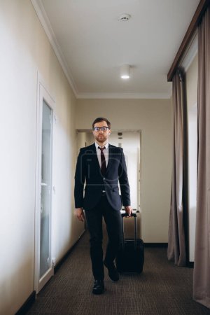 Téléchargez les photos : Homme d'affaires marchant avec des bagages dans un couloir de l'hôtel - en image libre de droit