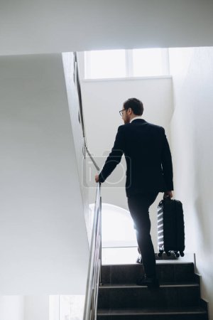 Téléchargez les photos : Un homme d'affaires avec une valise monte les escaliers de l'hôtel. - en image libre de droit