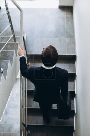 Téléchargez les photos : Un homme d'affaires avec une valise monte les escaliers de l'hôtel. Vue du dessus. - en image libre de droit