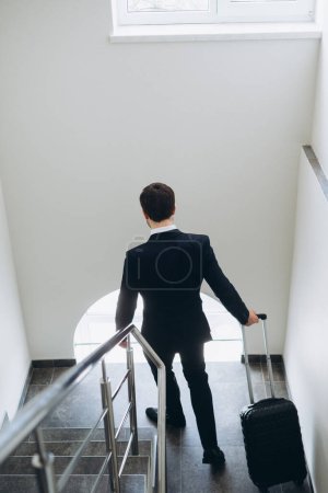 Téléchargez les photos : Un homme d'affaires avec une valise monte les escaliers de l'hôtel. Vue du dessus. - en image libre de droit