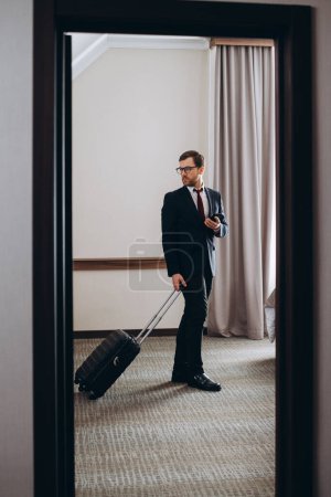 Téléchargez les photos : Un homme d'affaires avec une valise entre dans sa chambre d'hôtel. - en image libre de droit