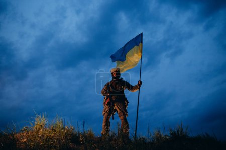 Photo for Armed Ukrainian warrior with blue and yellow flag in the evening - Royalty Free Image