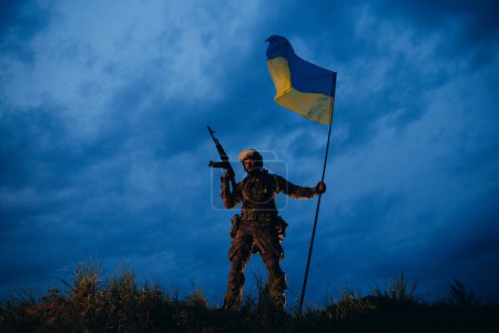 Bewaffneter ukrainischer Soldat hält nach der Schlacht eine Nationalflagge in der Hand 