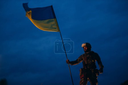 Photo for Portrait of male Ukrainian warrior holding a national flag in the evening - Royalty Free Image