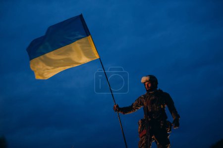 Photo for An evening photo of Ukrainian defender holding a national flag - Royalty Free Image