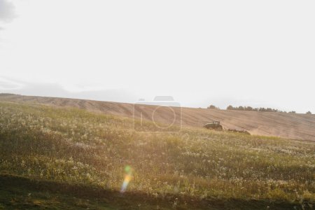 Foto de Un tractor moderno con una pesada grada de disco arrastrado arada un campo de trigo al atardecer. - Imagen libre de derechos