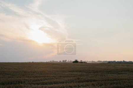 Foto de Un tractor moderno con una pesada grada de disco arrastrado arada un campo de trigo al atardecer. - Imagen libre de derechos