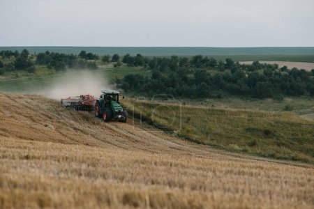 Foto de Un tractor arada un campo de trigo. El concepto del trabajo de un agricultor y la cosecha. - Imagen libre de derechos