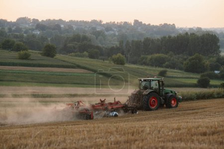 Téléchargez les photos : Un tracteur laboure un champ de blé. Le concept du travail de l'agriculteur et de la récolte. - en image libre de droit