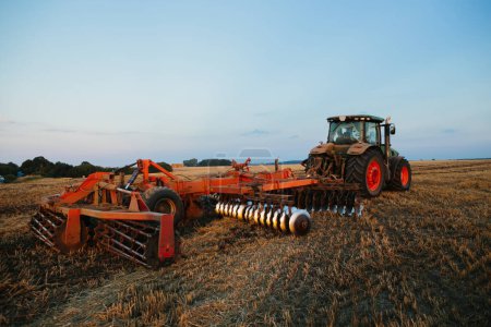 Téléchargez les photos : Un tracteur avec une grande herse à disques pour le travail du sol. Concept de travail agricole. - en image libre de droit