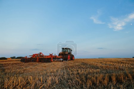 Photo for Modern tractor with a heavy trailed disc harrow works a wide hilly field. Autumn or spring agricultural campaign - Royalty Free Image