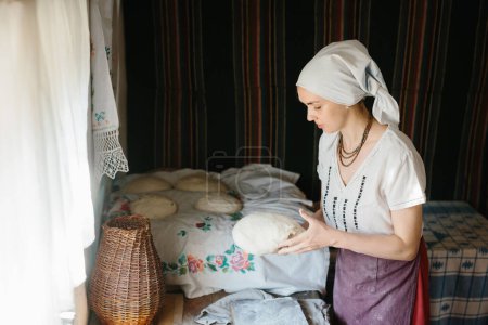Photo for A woman in a Ukrainian embroidered dress holds a raw loaf of bread in her hands. - Royalty Free Image