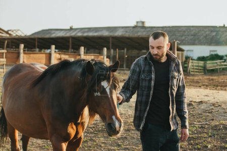 Photo for A young farmer works in a paddock with horses. A young man takes care of horses on a farm. - Royalty Free Image
