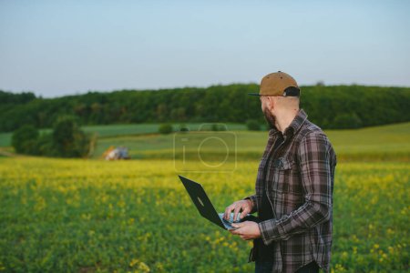 Photo for A farmer inspects field work. A man with a laptop monitors the work of a tractor in the field. - Royalty Free Image
