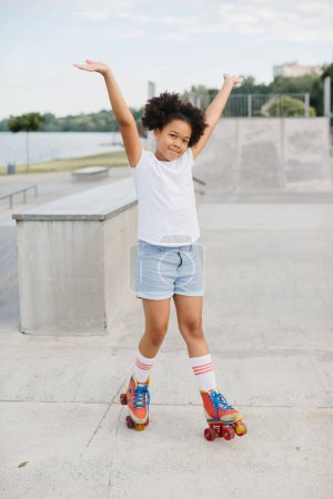 Foto de Linda niña afroamericana montando en patín en el parque de verano. Niño disfrutando del deporte al aire libre en el parque, niña divertida jugando en patín sobre ruedas en la carretera. deporte aprendizaje al aire libre concepto - Imagen libre de derechos