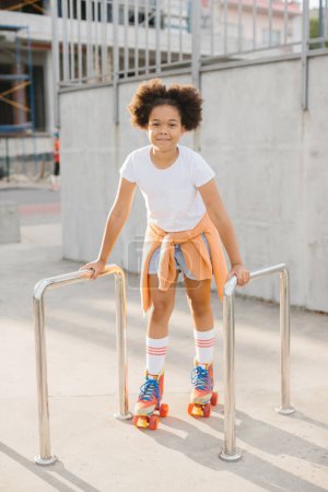 Foto de Chica joven afroamericana en patines que se divierten al aire libre. La chica sonríe mirando a la cámara. - Imagen libre de derechos