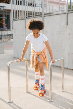 Téléchargez les photos : Afro-américaine jeune fille en patins à roulettes avoir du plaisir en plein air. - en image libre de droit