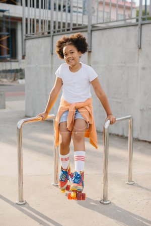 Foto de Chica joven afroamericana en patines que se divierten al aire libre. La chica sonríe mirando a la cámara. - Imagen libre de derechos