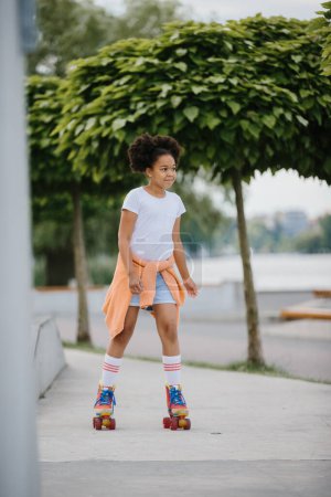 Photo for African American young girl roller skating outdoors, child playing on roller skates. - Royalty Free Image