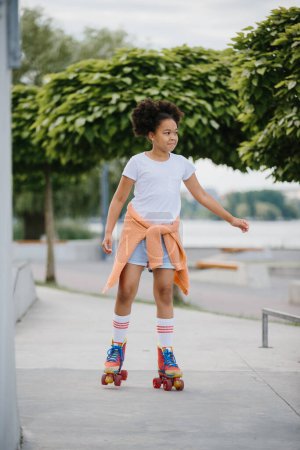 Foto de Niña afroamericana patinaje sobre ruedas al aire libre, niño jugando en patines. - Imagen libre de derechos