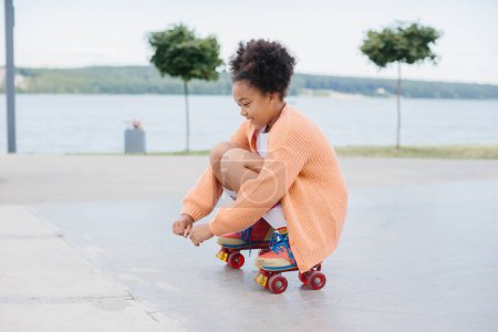 Téléchargez les photos : Afro-Américaine jeune fille patinage à roulettes en plein air, enfant jouant sur des patins à roulettes. - en image libre de droit