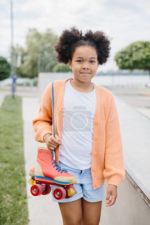 Foto de Una joven vino a patinar en el parque de skate. Chica afroamericana sosteniendo rodillos vintage atados con cordones. - Imagen libre de derechos