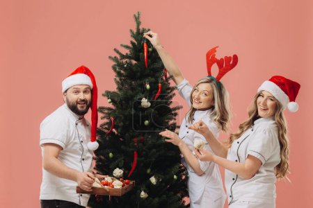 Téléchargez les photos : Le concept de cuisine et vacances de Noël. Un groupe de cuisiniers décore un arbre de Noël avec des légumes frais. - en image libre de droit