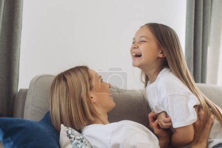 Téléchargez les photos : Mère et fille s'amusent à passer du temps libre ensemble à la maison à jouer et à se câliner. - en image libre de droit