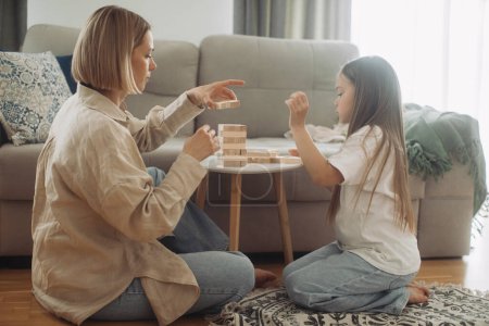 Téléchargez les photos : Une mère heureuse et sa petite fille s'amusent à jouer à un jeu de société. Mère et fille jouent Jenga dans le salon. - en image libre de droit