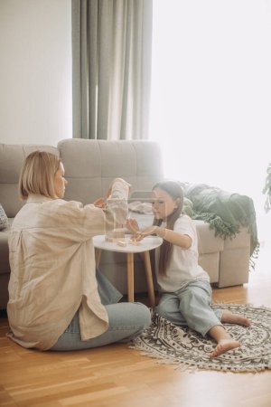 Photo for A happy mother and her little daughter have fun playing a board game. Mother and daughter play Jenga in the living room. - Royalty Free Image