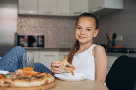 Foto de Mamá y su hija están comiendo deliciosa pizza en la cocina. - Imagen libre de derechos