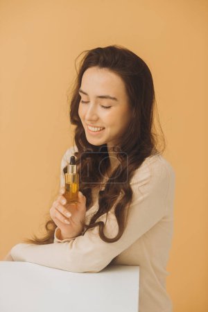 Téléchargez les photos : Soins de la peau. Portrait de beauté d'une femme tenant une bouteille compte-gouttes isolée sur fond beige. - en image libre de droit