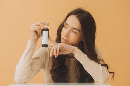 Photo for Photo mockup. Pretty brunette woman holding bottle of cosmetics isolated on beige background. - Royalty Free Image