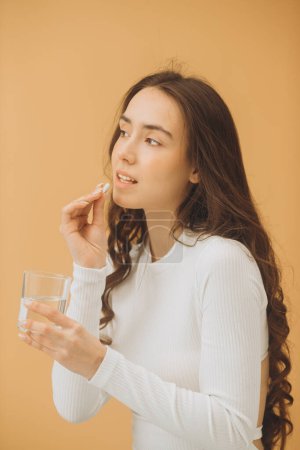Téléchargez les photos : Jolie jeune femme qui prend des vitamines. Une femme tient une pilule et un verre d'eau. - en image libre de droit