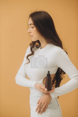 Foto de Retrato de belleza. Una hermosa chica con la piel limpia sostiene un tubo de maqueta en sus manos. Fondo beige. - Imagen libre de derechos