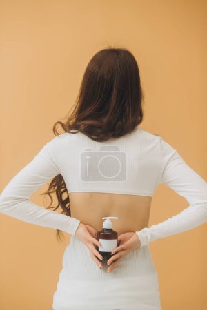 Photo for A woman holds a bottle of cosmetics in her hand, standing with her back to the camera. Cosmetics mockup. - Royalty Free Image