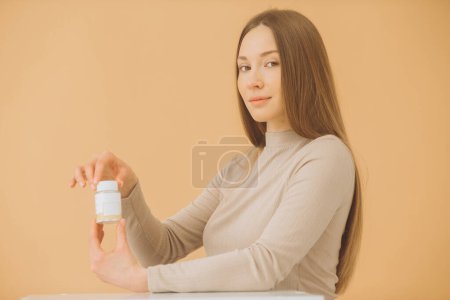 Téléchargez les photos : Attrayant femme tenant bouteille de vitamines ou de pilules isolées sur fond beige. - en image libre de droit