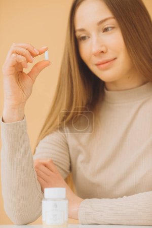 Téléchargez les photos : Attrayant femme tenant bouteille de vitamines ou de pilules isolées sur fond beige. - en image libre de droit