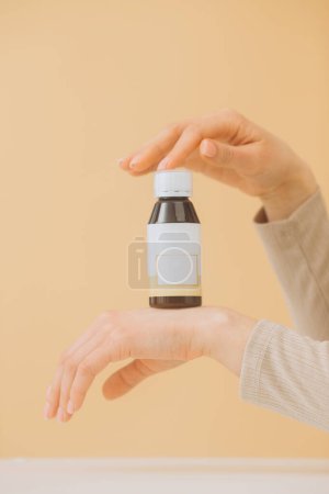 Téléchargez les photos : Une main féminine touche une bouteille de pilules sur un fond beige. - en image libre de droit